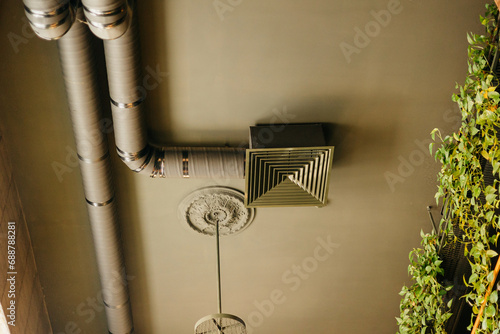 Part of interior of modern loft style restaurant. Bottom view on of grey ceiling with open ventilation pipes, moulding with chandelier, wall covered in vivid greenery ivy. Industrial style photo