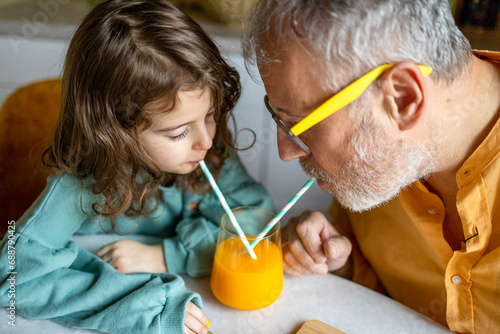 Senior man and girl drinking fruit juice on table photo
