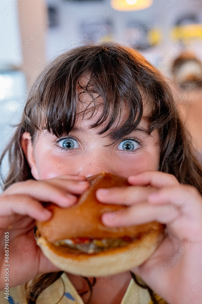 Closeup hands of hungry anonymous girl holding and eating delicious hamburger and looking at camera while spending leisure time in cafe Closeup hands of hungry anonymous girl holding and eating delicious hamburger and looking at camera while spending leisure time in cafe