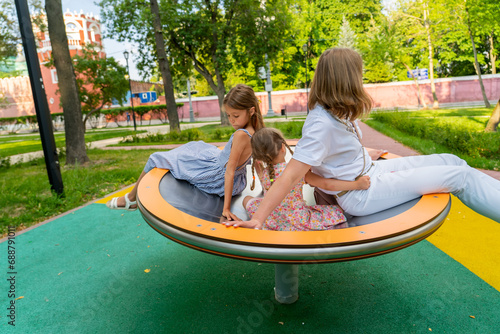 Happy mother spinning on carousel with two girls on modern merry go round on playground at park © sommersby