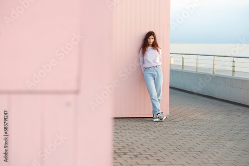 Young woman posing in front of the sea leaning against a pink wall