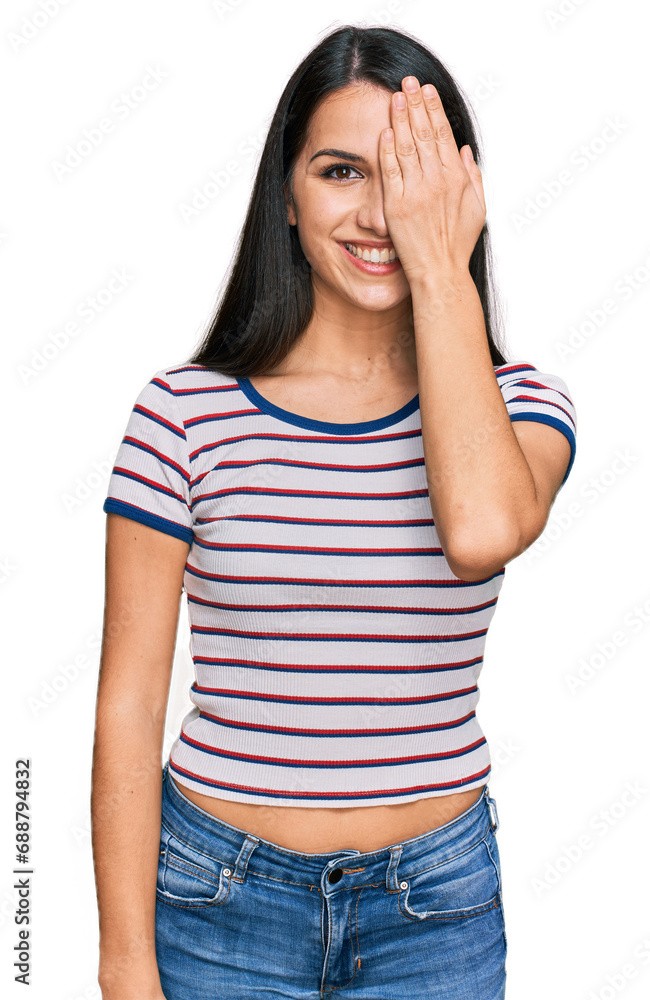 Young hispanic girl wearing casual striped t shirt covering one eye with hand, confident smile on face and surprise emotion. Young hispanic girl wearing casual striped t shirt covering one eye with hand, confident smile on face and surprise emotion.