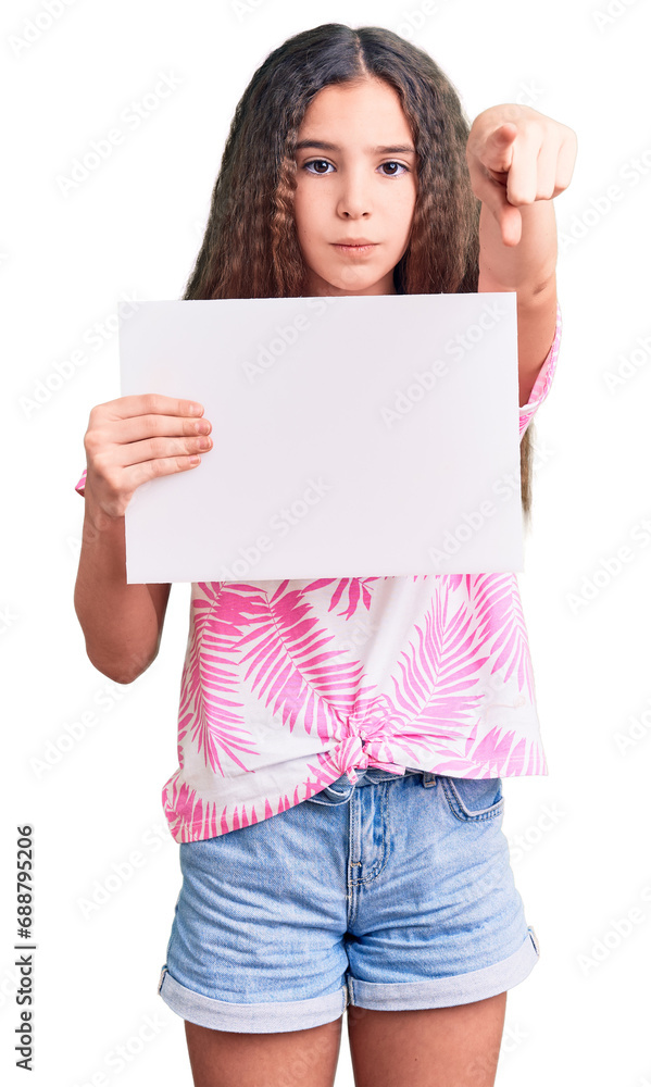 Cute hispanic child girl holding blank empty banner pointing with finger to the camera and to you, confident gesture looking serious Cute hispanic child girl holding blank empty banner pointing with finger to the camera and to you, confident gesture looking serious