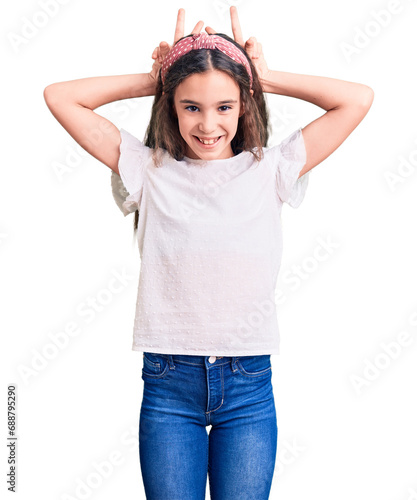Cute hispanic child girl wearing casual white tshirt posing funny and crazy with fingers on head as bunny ears, smiling cheerful