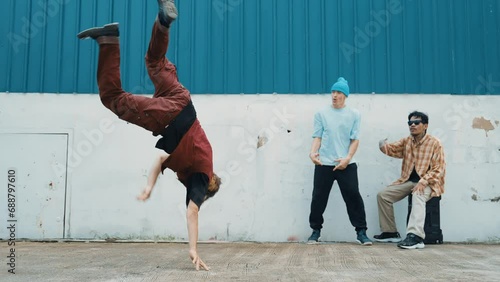 Young asian dancer dancing in hip hop style with multicultural friends cheering behind at wall. Attractive handsome man stretch arms at street with blue background. Outdoor sport 2024. hiphop.