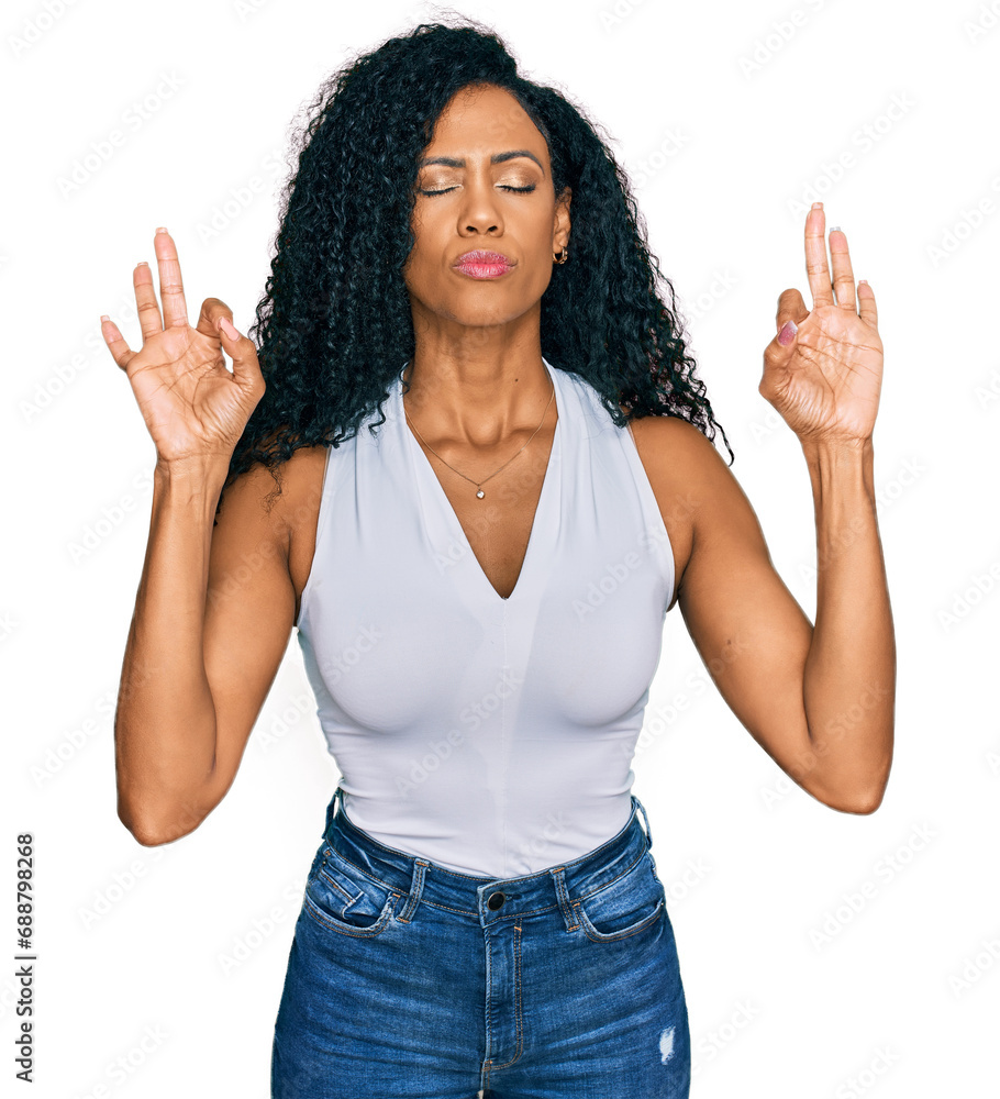 Middle age african american woman wearing casual style with sleeveless shirt relax and smiling with eyes closed doing meditation gesture with fingers. yoga concept. Middle age african american woman wearing casual style with sleeveless shirt relax and smiling with eyes closed doing meditation gesture with fingers. yoga concept.