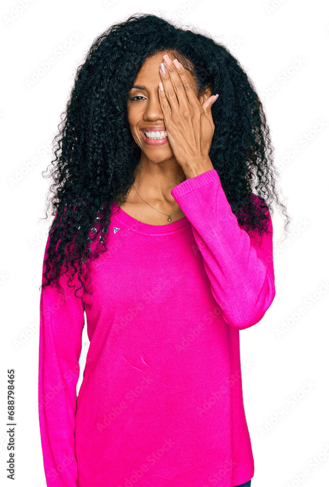 Middle age african american woman wearing casual clothes covering one eye with hand, confident smile on face and surprise emotion.