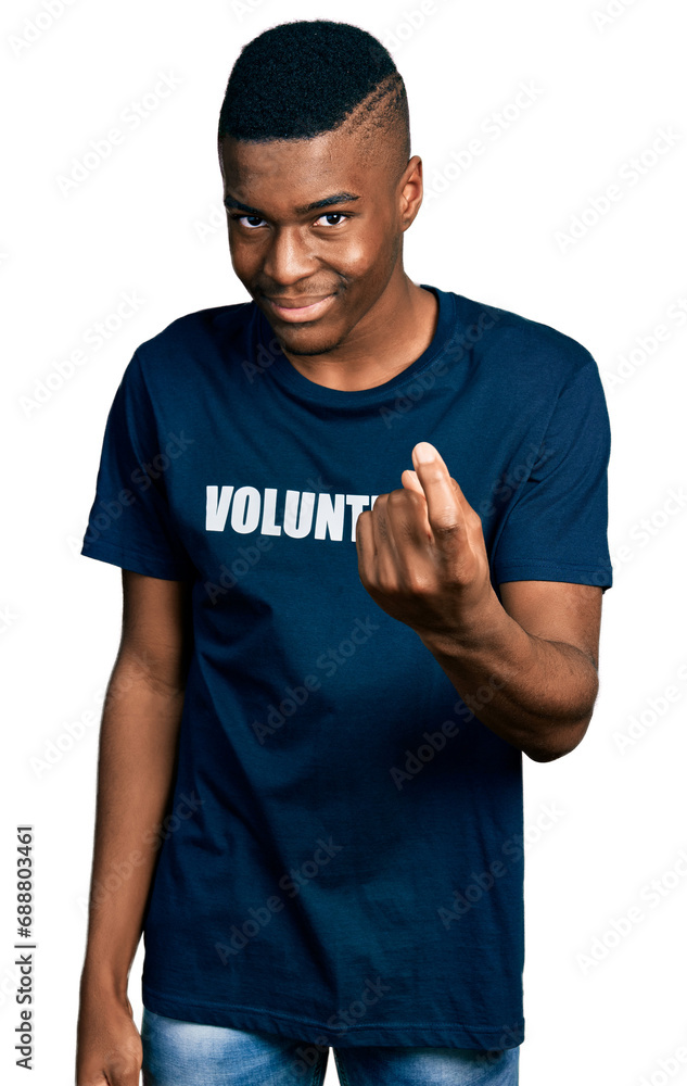 Young african american man wearing volunteer t shirt beckoning come here gesture with hand inviting welcoming happy and smiling Young african american man wearing volunteer t shirt beckoning come here gesture with hand inviting welcoming happy and smiling