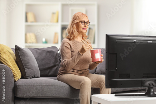 Woman on a couch in front of tv and eating noodles