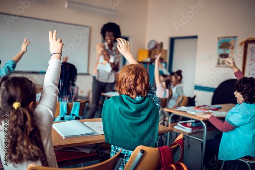 School students raising hands to answer in elementary classroom photo