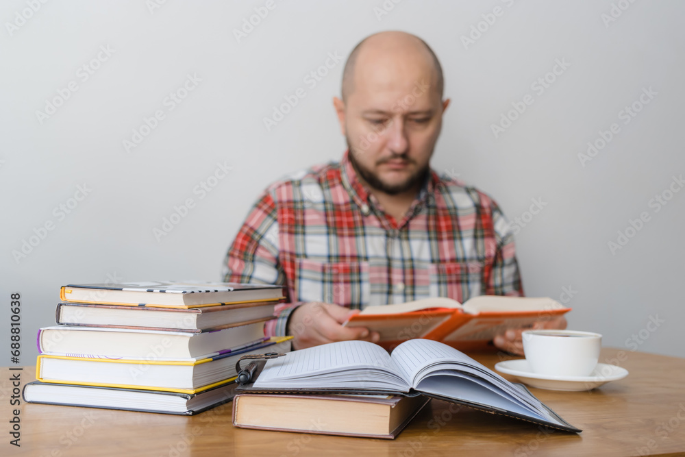 Man reading a book, studying or working, sitting at the table with stack of books and cup of coffee, focus on foreground Man reading a book, studying or working, sitting at the table with stack of books and cup of coffee, focus on foreground