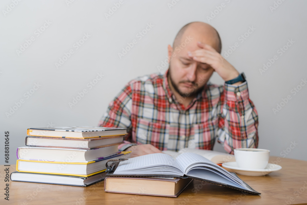 Man reading a book, studying or working, sitting at the table with stack of books and cup of coffee, focus on foreground Man reading a book, studying or working, sitting at the table with stack of books and cup of coffee, focus on foreground