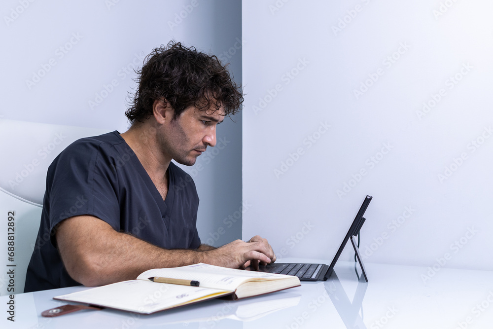 A male nurse is in the office looking at his laptop while calendaring his next clients. A male nurse is in the office looking at his laptop while calendaring his next clients.