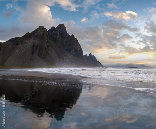 Sunrise Stokksnes cape sea beach and Vestrahorn Mountain with its reflection on wet black volcanic sand surface, Iceland. Amazing nature scenery, popular travel destination.