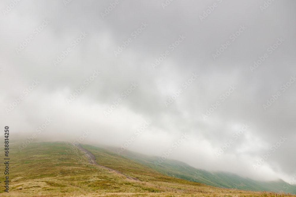 Photo of the summit of a mountain immersed in a cloud, with a damp autumn landscape.