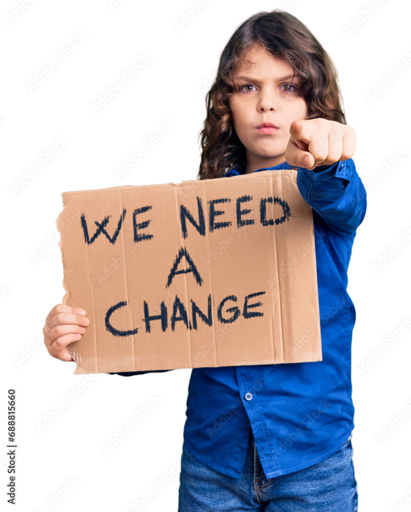 Cute hispanic child with long hair holding we need a change banner pointing with finger to the camera and to you, confident gesture looking serious Cute hispanic child with long hair holding we need a change banner pointing with finger to the camera and to you, confident gesture looking serious