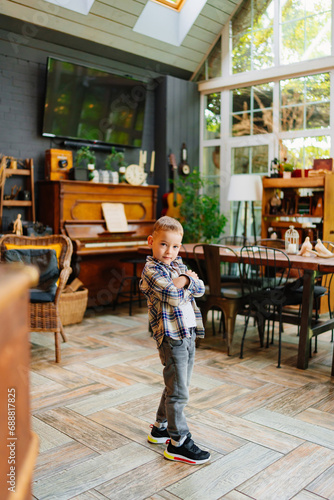 Funny little boy in plaid shirt and jeans in the interior of a country house. 