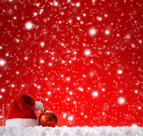 Christmas bauble and red Santa hat on white snow.