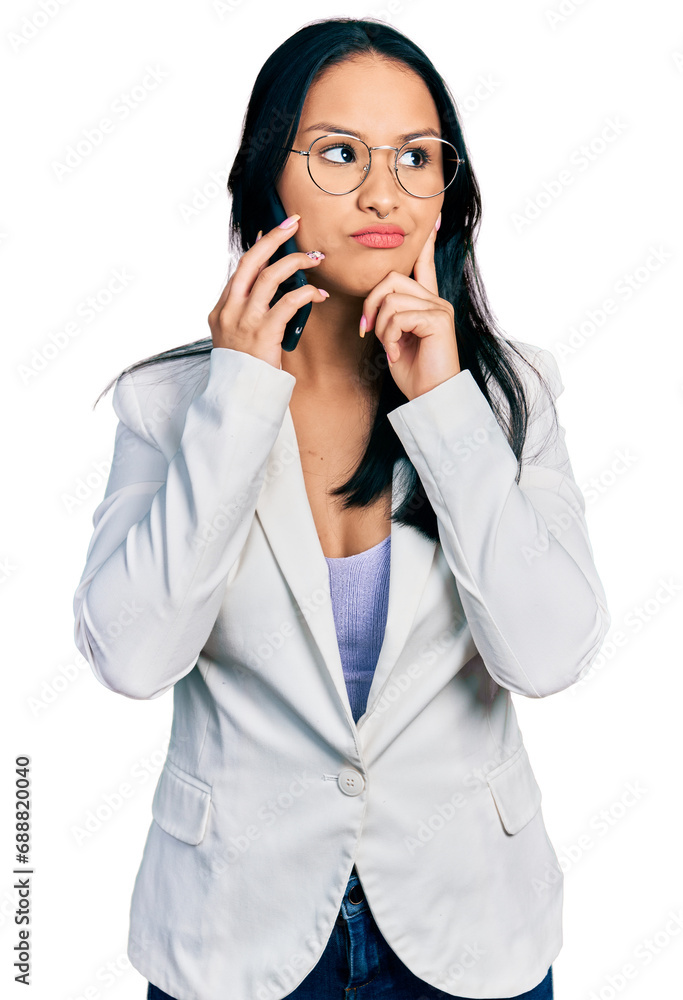 Beautiful hispanic woman with nose piercing having conversation talking on the smartphone serious face thinking about question with hand on chin, thoughtful about confusing idea