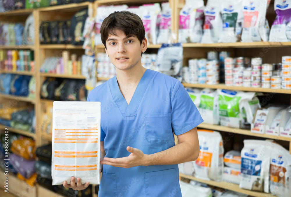 Successful smiling young veterinarian in blue uniform holding package of healthy natural dry pet food. Recommendation from professionals....