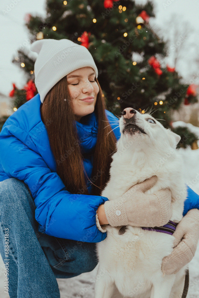 A beautiful young girl hugging her white dog in winter, Festive New Year's mood, happy woman with a dog at Christmas time A beautiful young girl hugging her white dog in winter, Festive New Year's mood, happy woman with a dog at Christmas time