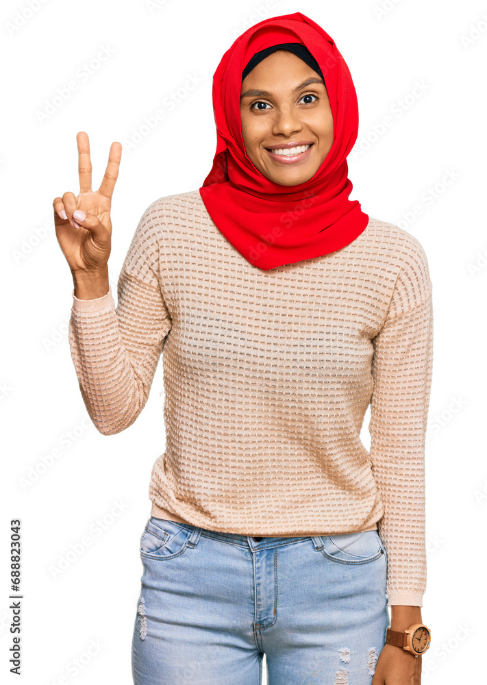 Young african american woman wearing traditional islamic hijab scarf smiling looking to the camera showing fingers doing victory sign. number two. Young african american woman wearing traditional islamic hijab scarf smiling looking to the camera showing fingers doing victory sign. number two.