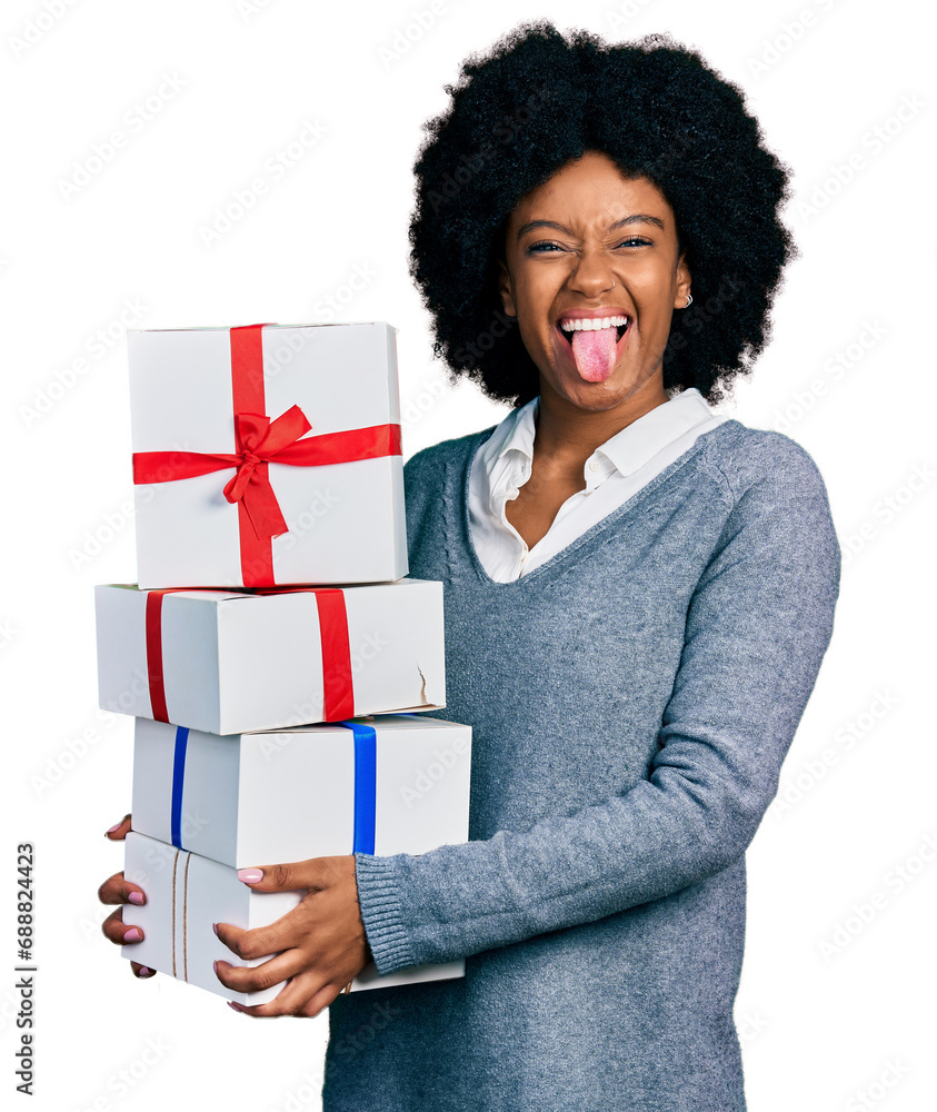 Young african american woman holding gifts sticking tongue out happy with funny expression. Young african american woman holding gifts sticking tongue out happy with funny expression.
