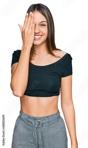 Young brunette woman wearing casual clothes covering one eye with hand  confident smile on face and surprise emotion.