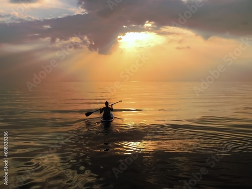 silhouette of a girl on a boat with an oar on the sea, in a calm, with a small surf, against the backdrop of dark clouds in the evening, before sunset © zakob