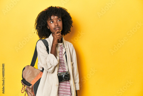 Teen girl with backpack, camera, ready for vacation looking sideways with doubtful and skeptical expression.