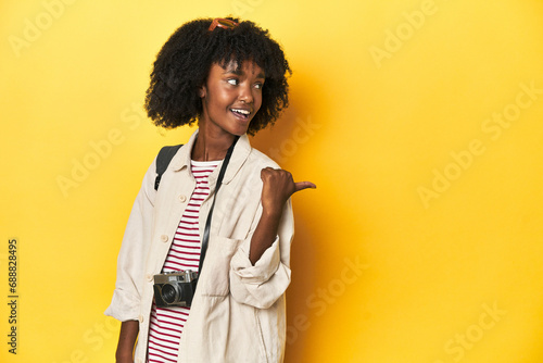 Teen girl with backpack, camera, ready for vacation points with thumb finger away, laughing and carefree.