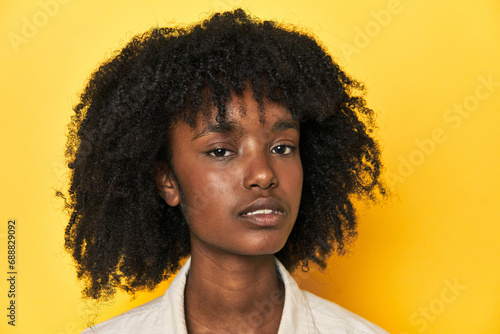 Close-up portrait of a beautiful African-American teenage girl on yellow backdrop.