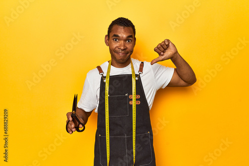 African American tailor with tools, yellow studio, showing a dislike gesture, thumbs down. Disagreement concept.