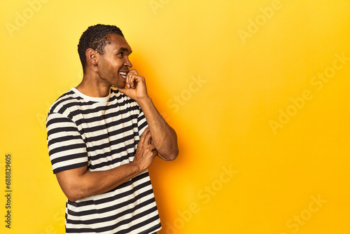 African American man in striped t-shirt, yellow studio, relaxed thinking about something looking at a copy space.