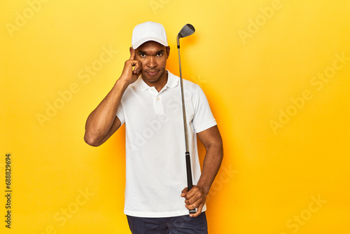 African American man golfer  yellow studio backdrop  pointing temple with finger  thinking  focused on a task.