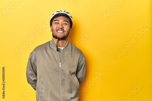 Asian man in bike helmet and gloves, yellow studio backdrop happy, smiling and cheerful.