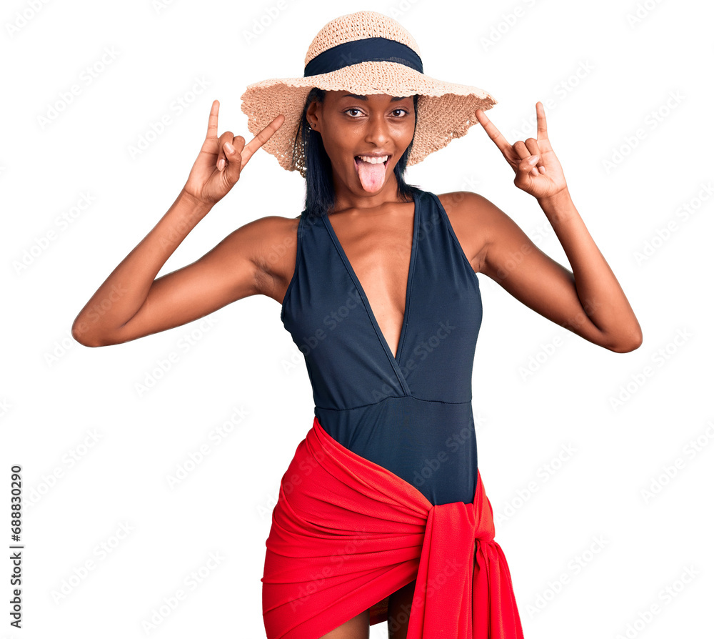 Young african american woman wearing swimsuit and summer hat shouting with crazy expression doing rock symbol with hands up. music star. heavy music concept. Young african american woman wearing swimsuit and summer hat shouting with crazy expression doing rock symbol with hands up. music star. heavy music concept.