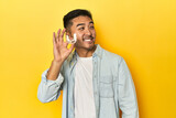 Asian man with invisible dental corrector, yellow studio backdrop looks aside smiling, cheerful and pleasant.