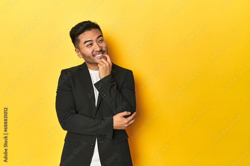 Asian man in black business jacket on yellow studio relaxed thinking about something looking at a copy space. Asian man in black business jacket on yellow studio relaxed thinking about something looking at a copy space.