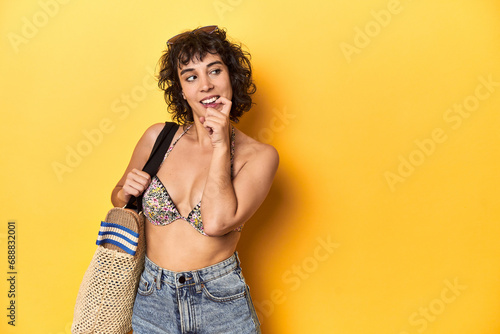 Caucasian woman in bikini with beach bag, studio relaxed thinking about something looking at a copy space.