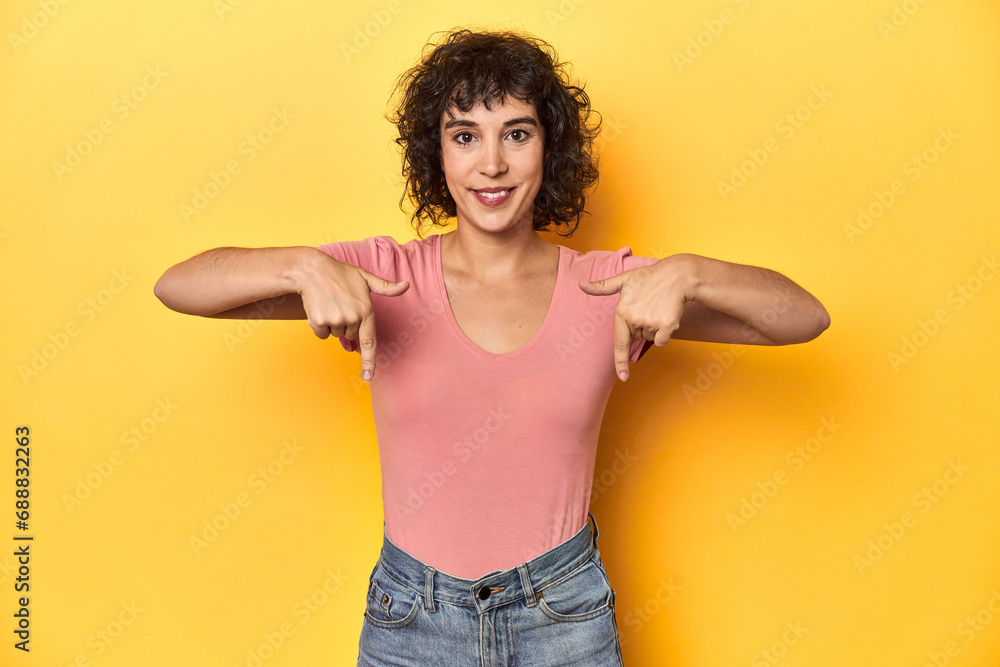 Curly-haired Caucasian woman in pink t-shirt points down with fingers, positive feeling. Curly-haired Caucasian woman in pink t-shirt points down with fingers, positive feeling.