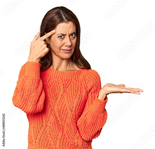 Elegant middle-aged Caucasian woman in studio setting holding and showing a product on hand.