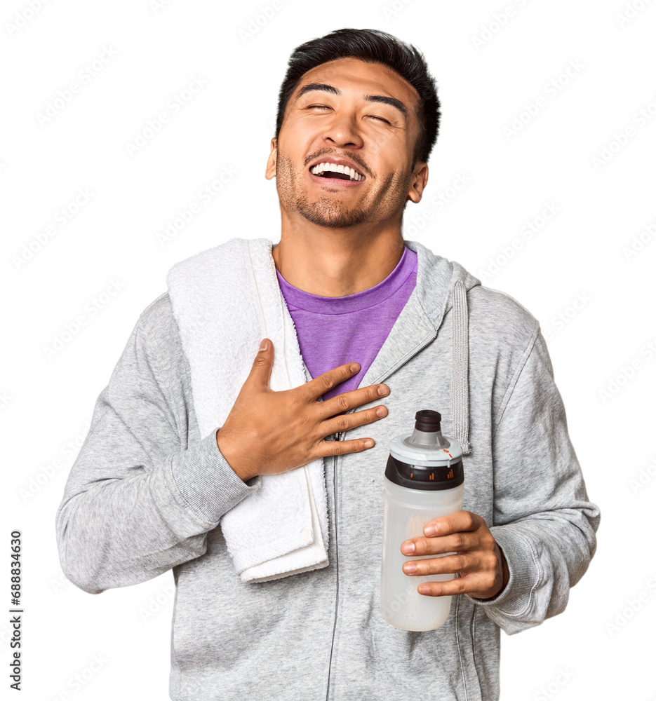 Chinese man with sportswear, towel, bottle in studio laughs out loudly keeping hand on chest. Chinese man with sportswear, towel, bottle in studio laughs out loudly keeping hand on chest.