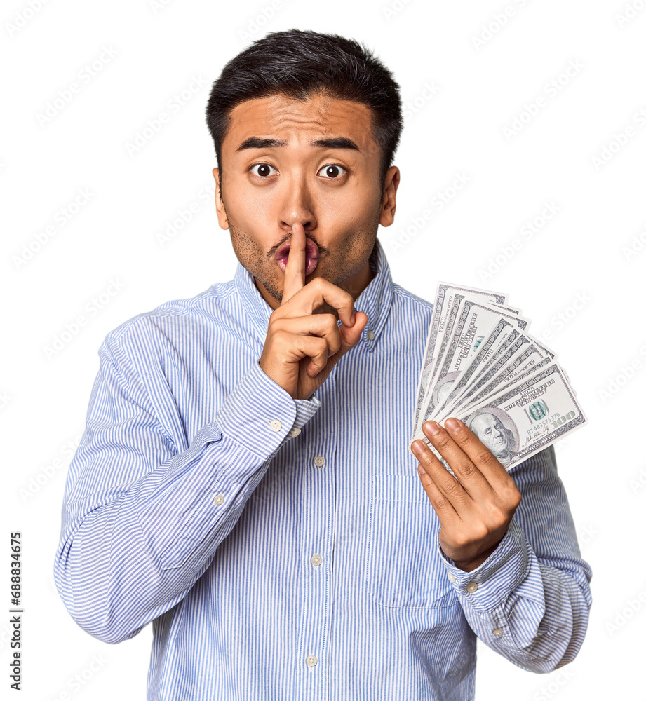 Young Chinese man holding dollar bills in studio keeping a secret or asking for silence. Young Chinese man holding dollar bills in studio keeping a secret or asking for silence.