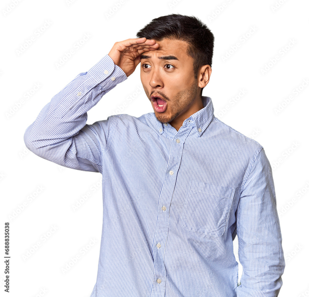 Young Chinese man in studio background looking far away keeping hand on forehead. Young Chinese man in studio background looking far away keeping hand on forehead.