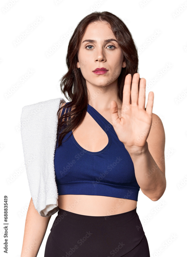 Athletic young Caucasian woman with towel in studio standing with outstretched hand showing stop sign, preventing you. Athletic young Caucasian woman with towel in studio standing with outstretched hand showing stop sign, preventing you.