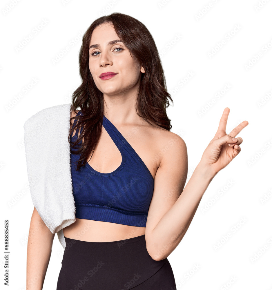 Athletic young Caucasian woman with towel in studio joyful and carefree showing a peace symbol with fingers. Athletic young Caucasian woman with towel in studio joyful and carefree showing a peace symbol with fingers.