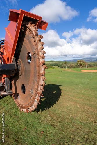 A giant rockwheel, drum of a trench digging machine, earth saw for irrigation and cable laying project on the green grass of a golf curse, Kauai, Hawaii