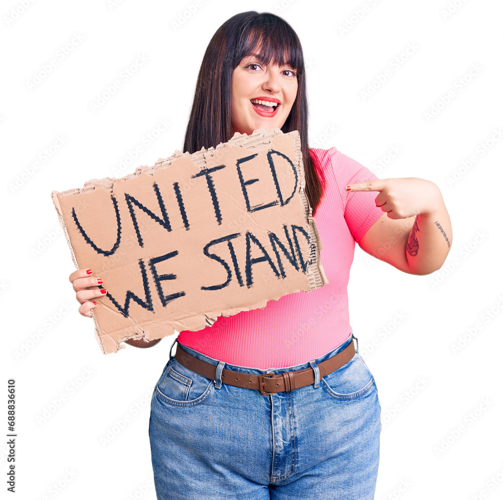 Young plus size woman holding united we stand banner smiling happy pointing with hand and finger Young plus size woman holding united we stand banner smiling happy pointing with hand and finger