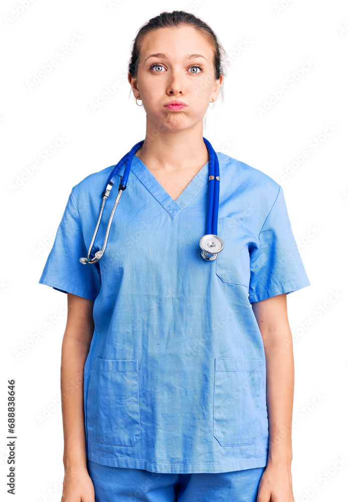 Young beautiful blonde woman wearing doctor uniform and stethoscope puffing cheeks with funny face. mouth inflated with air, crazy expression. Young beautiful blonde woman wearing doctor uniform and stethoscope puffing cheeks with funny face. mouth inflated with air, crazy expression.